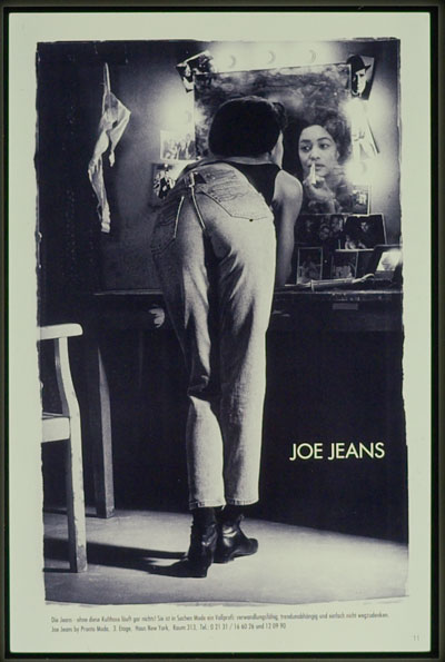 Eine Frau steht vor einem Spiegel und schminkt sich. Sie trägt eine Jeans von