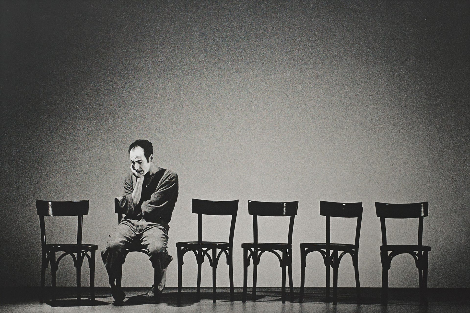 Ein Mann sitzt auf einem von sechs Stühlen. Er ist alleine und wirkt nachdenklich und traurig.