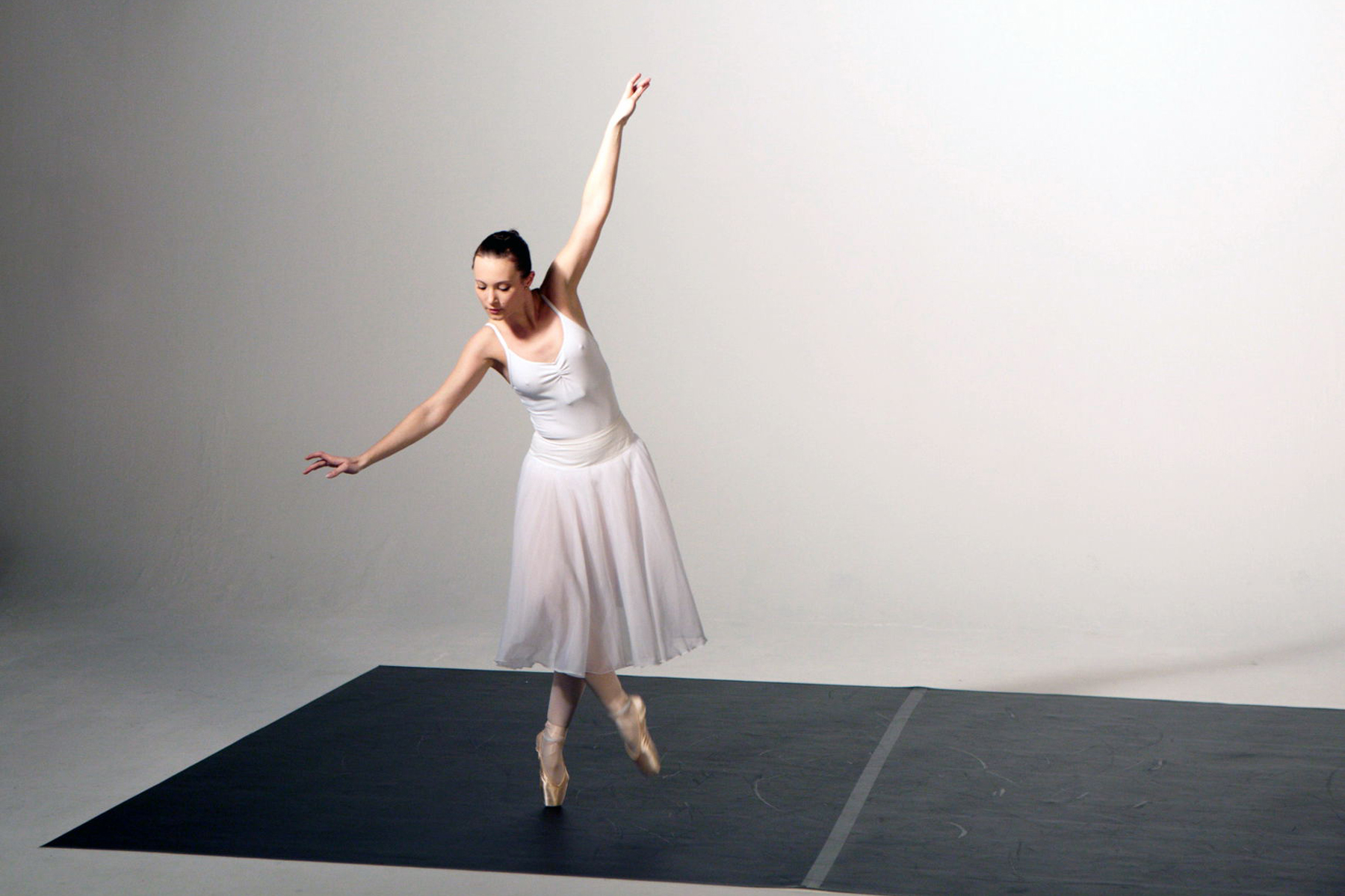 Eine Frau in einem weißen Kleid und Ballettschuhen tanzt in einem Studio. Die Bilder wurden für ein freies Filmprojekt im Studio Saibou in Köln aufgenommen.